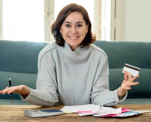 Young attractive latin business woman with credit card and calculator accounting costs, charges, taxes and mortgage on sofa at home paying bills looking happy and relaxed with own business success